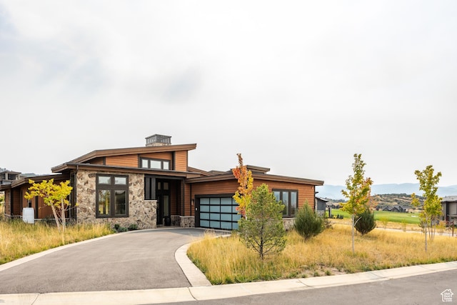 contemporary house featuring stone siding, aphalt driveway, a chimney, an attached garage, and a mountain view