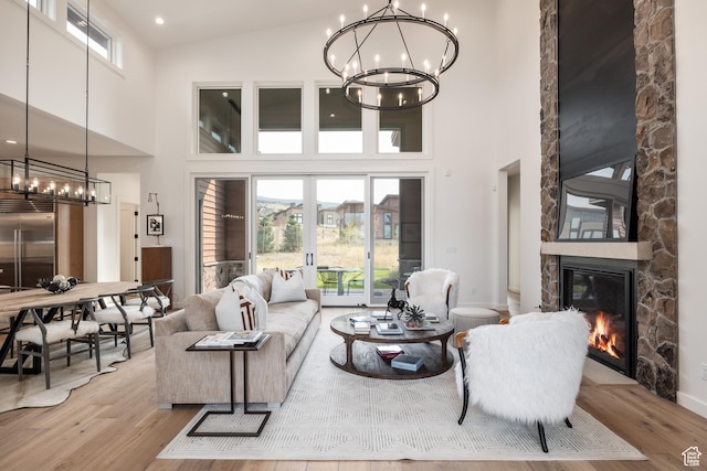 living room featuring a stone fireplace, a wealth of natural light, wood finished floors, and a chandelier