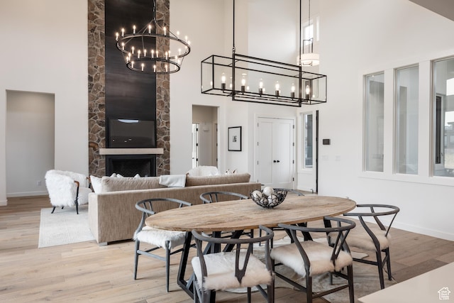 dining room with baseboards, a towering ceiling, a fireplace, light wood-style floors, and a notable chandelier