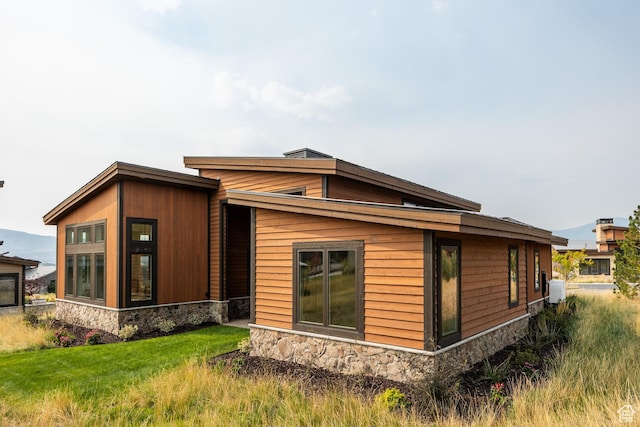 back of property featuring stone siding and a yard