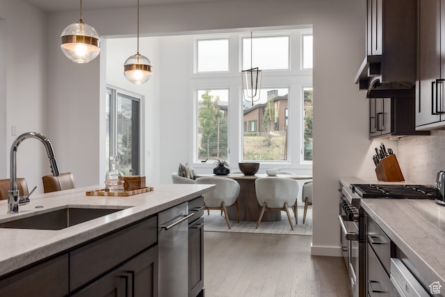 kitchen featuring stainless steel range with gas stovetop, decorative light fixtures, light stone countertops, dark wood-type flooring, and sink