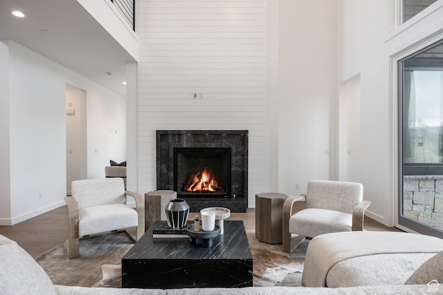 living room with a high end fireplace, a towering ceiling, and hardwood / wood-style floors