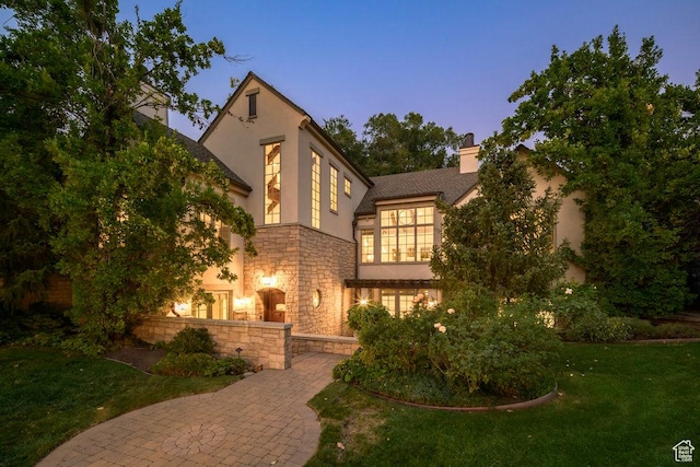 view of front facade featuring a lawn, a chimney, stucco siding, and stone siding