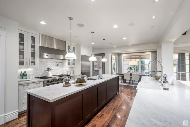 kitchen with wall chimney exhaust hood, tasteful backsplash, a center island with sink, a sink, and high quality appliances