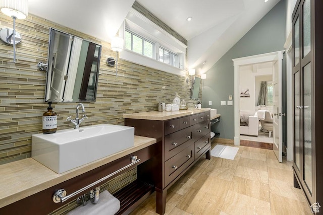ensuite bathroom featuring decorative backsplash, two vanities, lofted ceiling, a sink, and ensuite bath