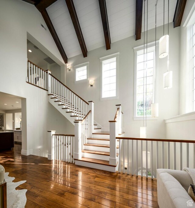 stairs with wood-type flooring, high vaulted ceiling, and beam ceiling