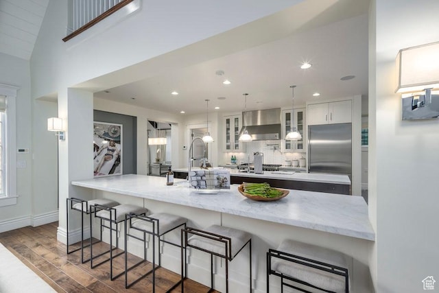 kitchen featuring tasteful backsplash, wall chimney exhaust hood, wood finished floors, glass insert cabinets, and stainless steel appliances