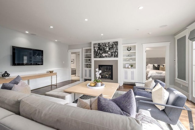 living area featuring wood finished floors, a glass covered fireplace, recessed lighting, built in features, and wainscoting