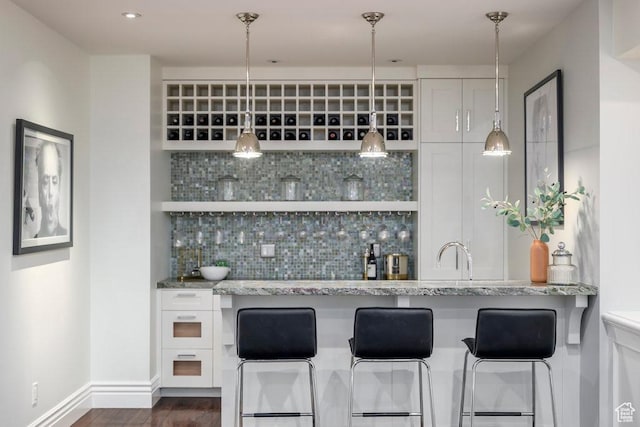 bar with baseboards, wet bar, a sink, dark wood-style floors, and backsplash