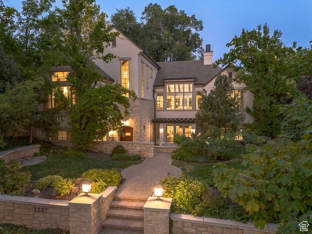 view of front of home with stone siding, a chimney, and stucco siding