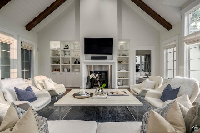 living area featuring high vaulted ceiling, built in features, beamed ceiling, and a glass covered fireplace