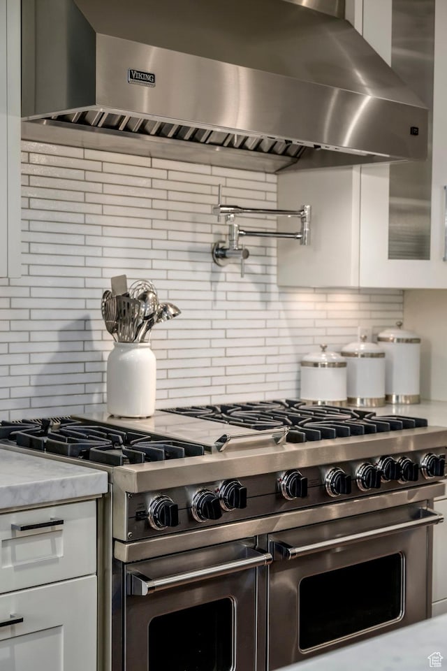 kitchen with double oven range, wall chimney exhaust hood, and white cabinets