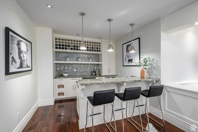 bar featuring baseboards, bar area, tasteful backsplash, dark wood-type flooring, and decorative light fixtures