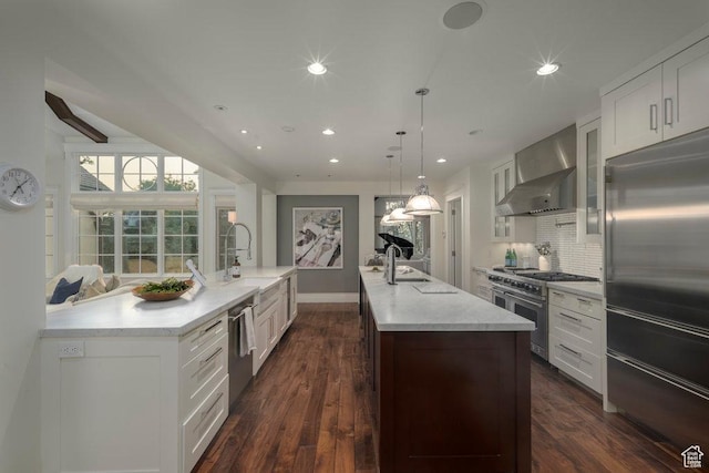 kitchen featuring dark wood finished floors, a large island with sink, high quality appliances, and wall chimney exhaust hood