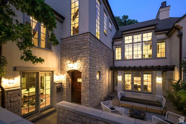 rear view of property with a chimney, stucco siding, stone siding, and french doors