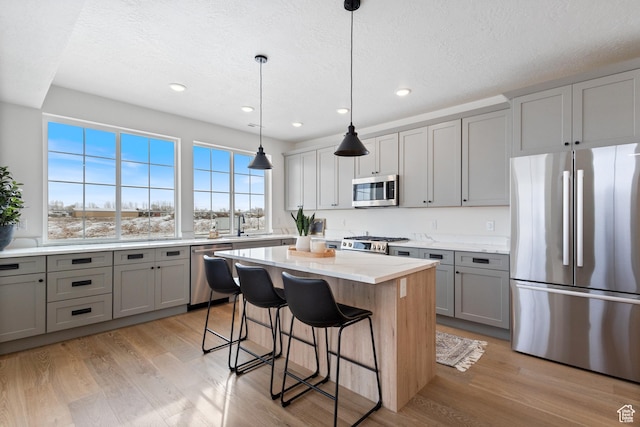 kitchen featuring a kitchen breakfast bar, light wood-type flooring, gray cabinets, a kitchen island, and stainless steel appliances