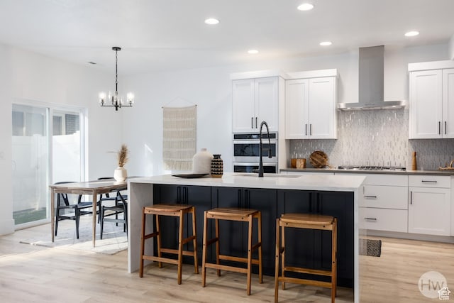 608 E Simpson Ave S, Salt Lake City, UT 84106 - kitchen featuring stainless steel appliances, a center island with sink, light wood finished floors, and wall chimney exhaust hood