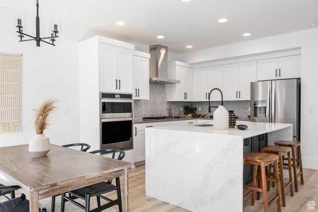 608 E Simpson Ave S, Salt Lake City, UT 84106 - kitchen featuring a sink, wall chimney range hood, appliances with stainless steel finishes, decorative backsplash, and a center island with sink