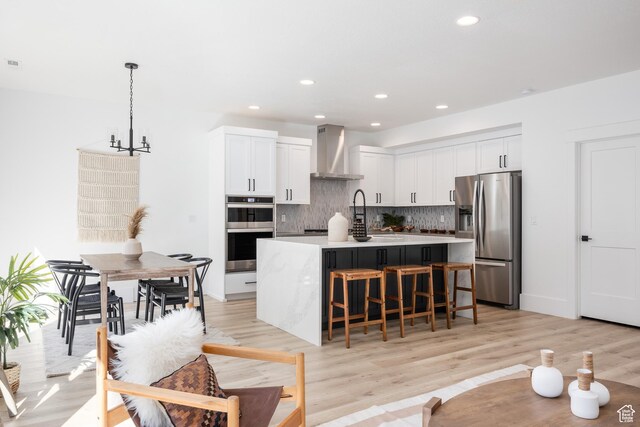 608 E Simpson Ave S, Salt Lake City, UT 84106 - kitchen featuring a center island with sink, decorative backsplash, a breakfast bar, stainless steel appliances, and wall chimney range hood