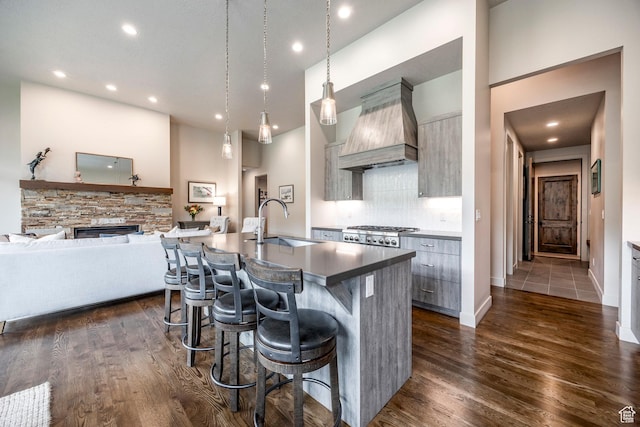kitchen with a sink, a breakfast bar, a center island with sink, premium range hood, and dark wood-type flooring