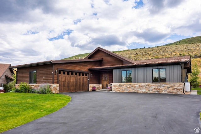 view of front facade featuring a front lawn, an attached garage, driveway, stone siding, and a mountain view