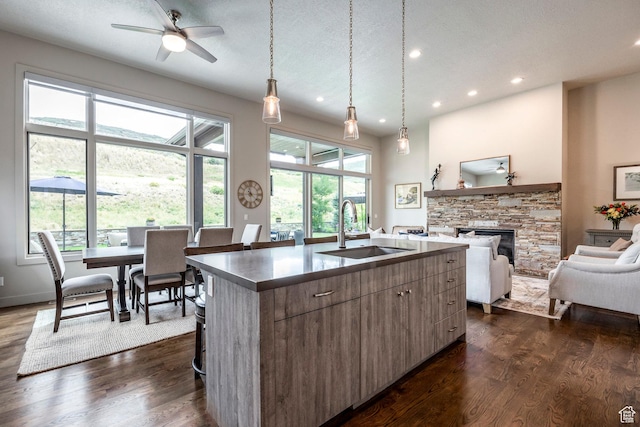 kitchen with dark wood finished floors, an island with sink, a sink, a fireplace, and open floor plan
