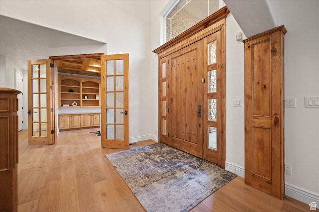 foyer featuring baseboards, light wood-style floors, and french doors