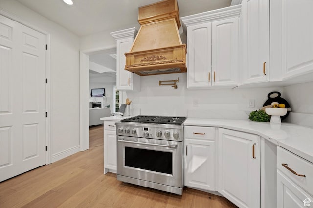 kitchen with white cabinets, premium range hood, high end stainless steel range, light wood-style floors, and light stone counters