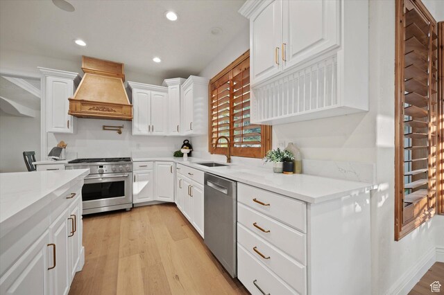 kitchen with premium range hood, a sink, white cabinets, light wood-style flooring, and appliances with stainless steel finishes