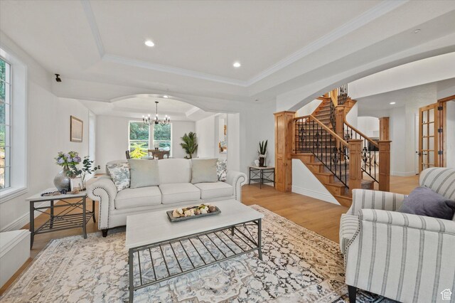 living area with a tray ceiling, stairway, light wood-style flooring, arched walkways, and an inviting chandelier