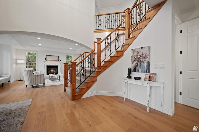 stairs with arched walkways, a glass covered fireplace, baseboards, and wood finished floors