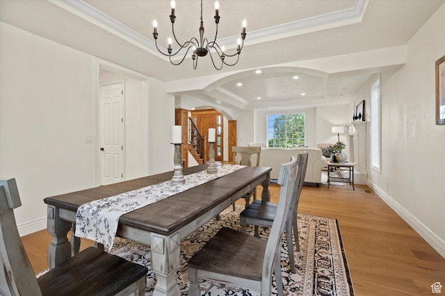 dining room featuring crown molding, light wood finished floors, arched walkways, a tray ceiling, and a notable chandelier