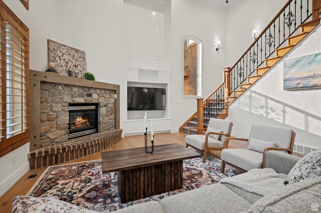 living room with stairway, a high ceiling, wood finished floors, a stone fireplace, and baseboards