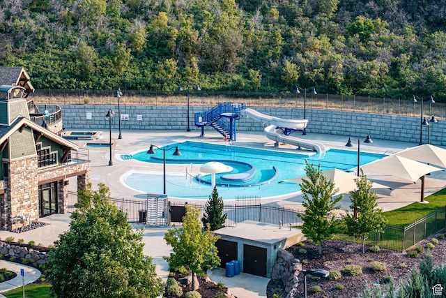 community pool with a water slide, fence, and a patio area