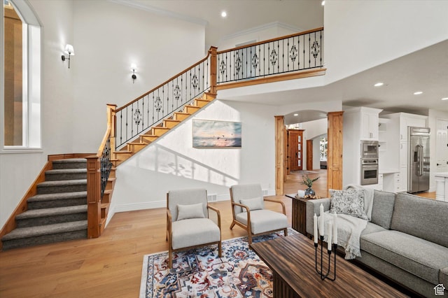 living area with light wood finished floors, baseboards, stairs, arched walkways, and a high ceiling