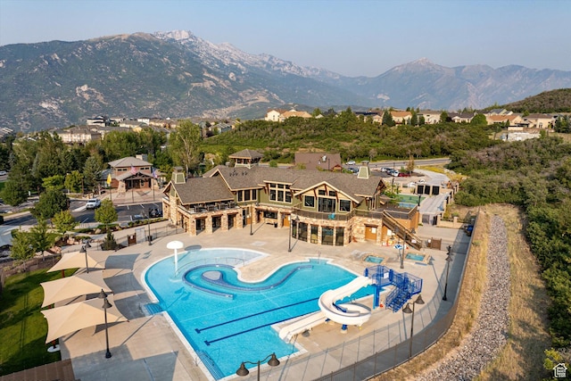 pool with a mountain view, fence, a water slide, and a patio area