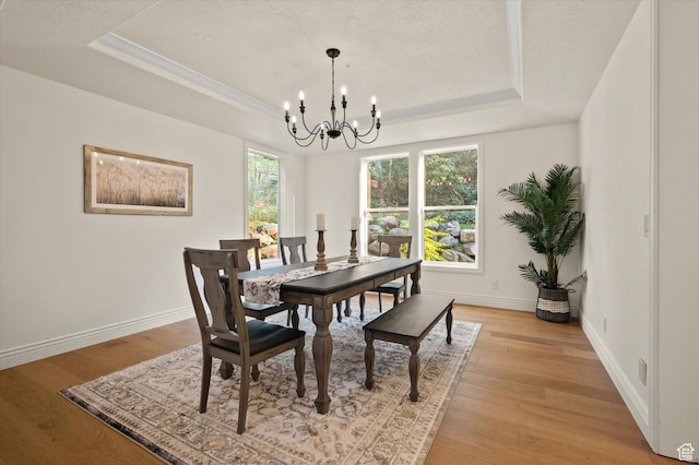 dining space with a chandelier, a raised ceiling, a textured ceiling, light wood-type flooring, and baseboards