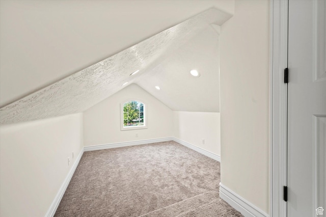 additional living space featuring carpet flooring, baseboards, lofted ceiling, and a textured ceiling