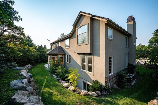 view of home's exterior featuring central air condition unit, stucco siding, a yard, and a chimney