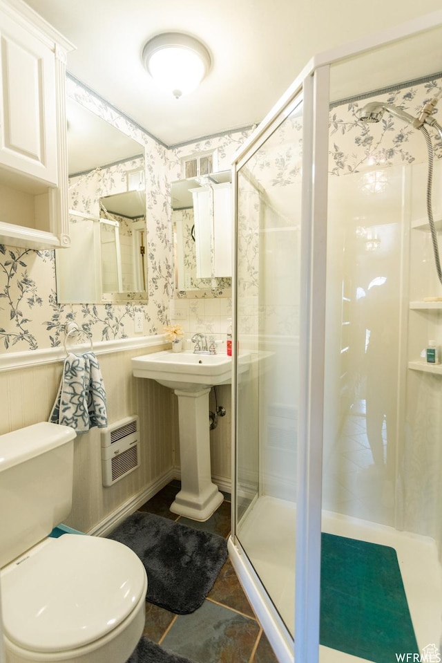 bathroom with toilet, a wainscoted wall, heating unit, a stall shower, and wallpapered walls
