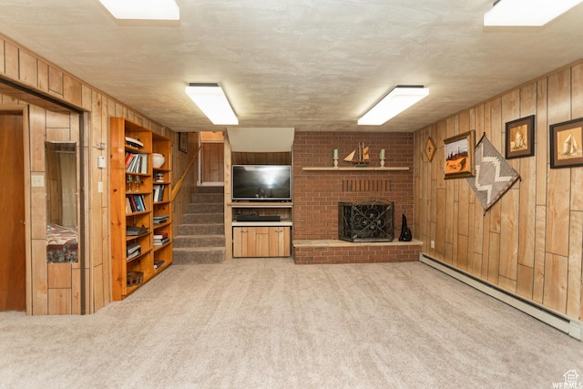 unfurnished living room featuring a fireplace, stairway, baseboard heating, carpet flooring, and wooden walls