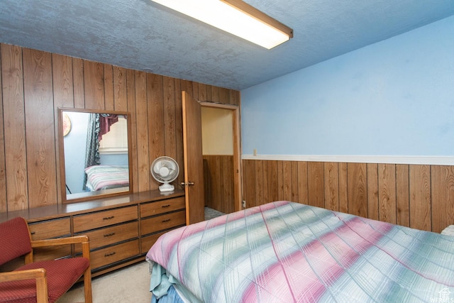 carpeted bedroom featuring wainscoting, wooden walls, and a textured ceiling