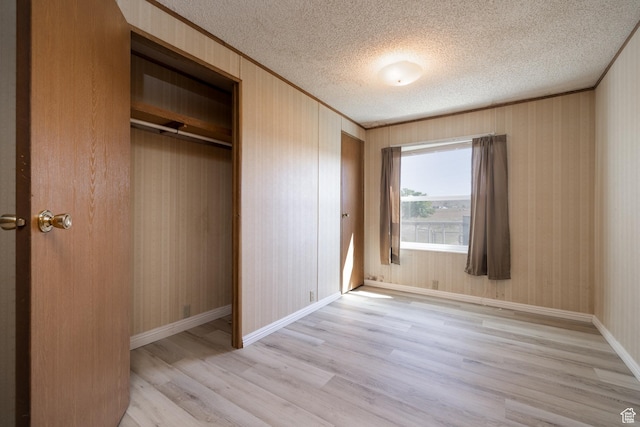 unfurnished bedroom with a textured ceiling, ornamental molding, baseboards, and light wood-style floors