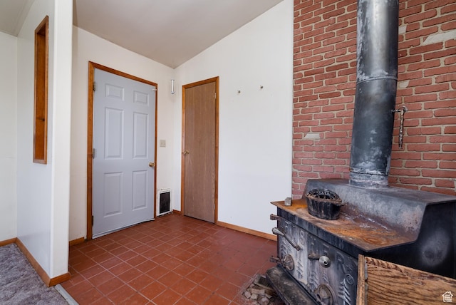 foyer with a wood stove, brick wall, and baseboards