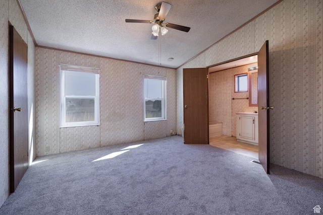 unfurnished bedroom with a textured ceiling, carpet flooring, vaulted ceiling, wallpapered walls, and crown molding