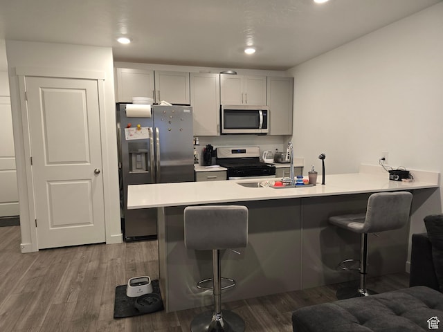 kitchen featuring wood finished floors, a peninsula, a breakfast bar area, and appliances with stainless steel finishes
