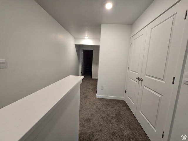 hallway with dark colored carpet and baseboards
