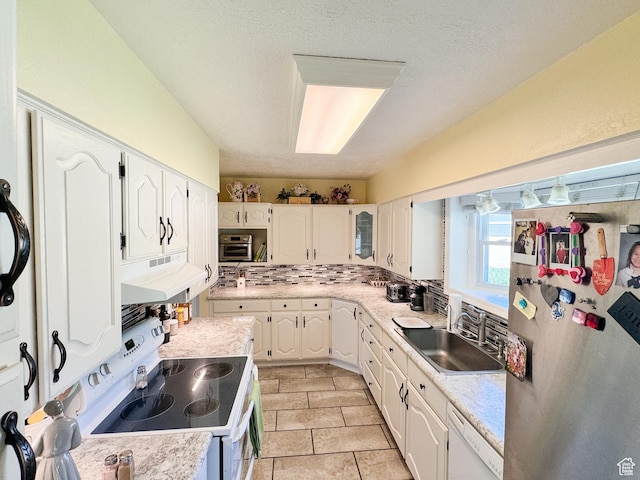 kitchen with a sink, under cabinet range hood, white appliances, white cabinets, and light countertops