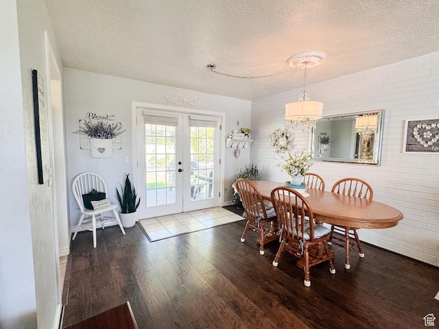 dining room with wood finished floors, brick wall, an inviting chandelier, french doors, and a textured ceiling