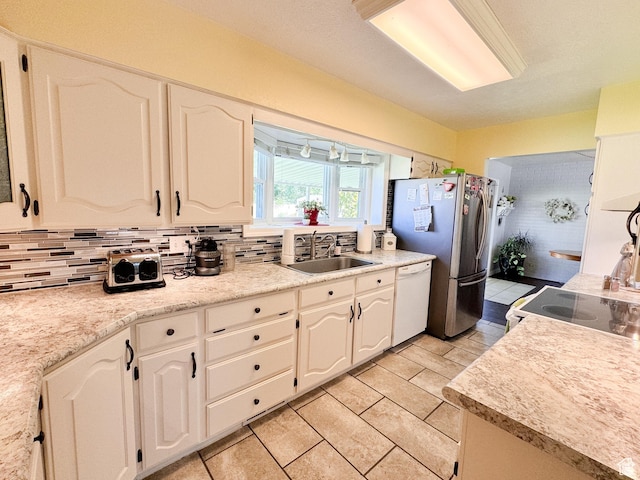 kitchen featuring backsplash, dishwasher, freestanding refrigerator, white cabinetry, and a sink